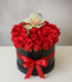 Arreglo de rosas rojas en caja redonda negra con lazo rojo y una orquídea blanca encima sobre fondo neutro