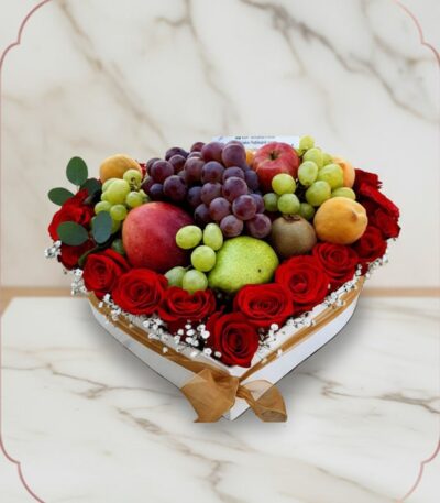 Arreglo floral ARMANI con frutas frescas variadas y rosas rojas dispuestas en una caja blanca en forma de corazón, ideal para
