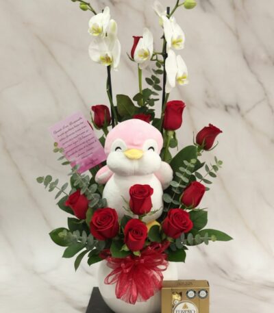 Arreglo floral ALICE con orquídeas blancas, rosas rojas frescas, peluche de pingüino rosa y chocolates Ferrero Rocher, ideal