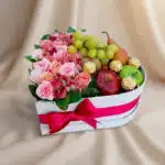 Arreglo AMOS en caja corazón con rosas rosadas, alstroemerias, uvas, manzanas, pera y chocolates Ferrero Rocher, ideal para r