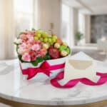 Arreglo floral AMOS en caja corazón con rosas, alstroemerias, frutas frescas y chocolates Ferrero Rocher, sobre mesa de mármo