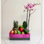 Arreglo ANTONELLO con orquídea Phalaenopsis rosa y frutas frescas como piña, manzanas, kiwis y mangos, presentado en una caja