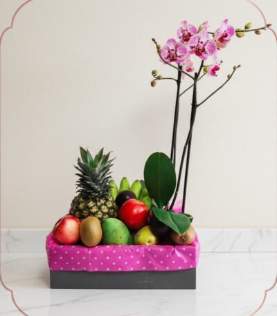 Arreglo ANTONELLO con orquídea Phalaenopsis rosa y frutas frescas como piña, manzanas, kiwis y mangos, presentado en una caja