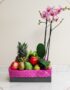 Arreglo ANTONELLO con orquídea Phalaenopsis rosa y frutas frescas como piña, manzanas, kiwis y mangos, presentado en una caja