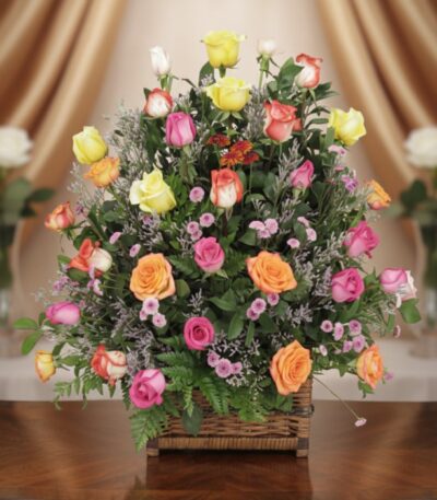 Arreglo floral DONNIA en cesta de mimbre con 34 rosas de colores variados (rosas, amarillas, naranjas) y follaje verde, sobre