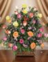 Arreglo floral DONNIA en cesta de mimbre con 34 rosas de colores variados (rosas, amarillas, naranjas) y follaje verde, sobre