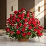 Arreglo Floral Amor Gigante con rosas rojas frescas y follaje verde en una cesta de mimbre, sobre una superficie de mármol pu