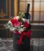 Arreglo floral BENTO con rosas rojas y rosadas, follaje verde y una botella de vino tinto en una caja negra con lazo rojo, so