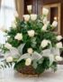 Arreglo floral de rosas blancas y orquídeas en una cesta de mimbre con lazo blanco, sobre una mesa de mármol en un entorno el