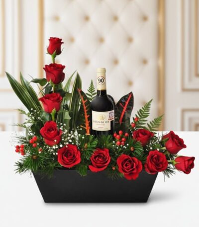 Arreglo floral CINZIA con 12 rosas rojas frescas, follaje verde variado y una botella de vino tinto, presentado en una base n