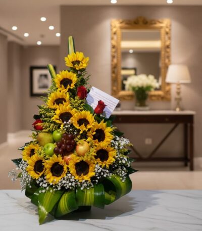 Arreglo floral dorado con girasoles, rosas rojas, uvas, manzanas y peras verdes, sobre una mesa de mármol en un elegante reci