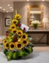 Arreglo floral dorado con girasoles, rosas rojas, uvas, manzanas y peras verdes, sobre una mesa de mármol en un elegante reci