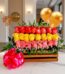Arreglo floral Escala con rosas rojas, amarillas y rosadas en caja de madera, con globos dorados y lazo rosa, sobre mesa de m