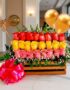 Arreglo floral Escala con rosas rojas, amarillas y rosadas en caja de madera, con globos dorados y lazo rosa, sobre mesa de m