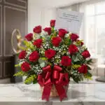 Arreglo floral Escarlata con rosas rojas vibrantes, follaje verde y flores blancas, presentado en una cesta de mimbre con un