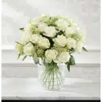 Arreglo floral Estefanía con 24 rosas blancas frescas en un jarrón de cristal sobre una mesa de mármol, con un fondo elegante