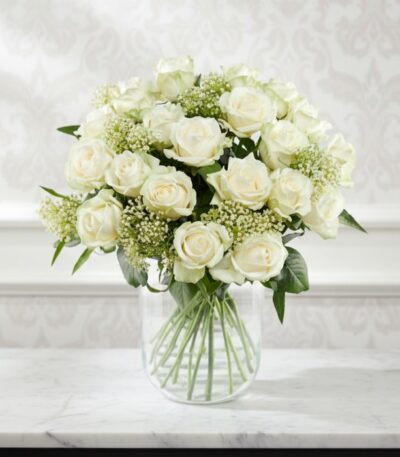 Arreglo floral Estefanía con 24 rosas blancas frescas en un jarrón de cristal sobre una mesa de mármol, con un fondo elegante