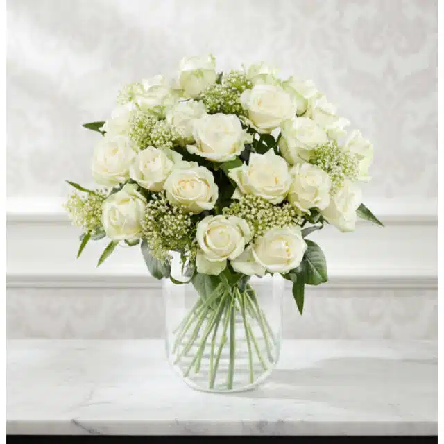 Arreglo floral Estefanía con 24 rosas blancas frescas en un jarrón de cristal sobre una mesa de mármol, con un fondo elegante