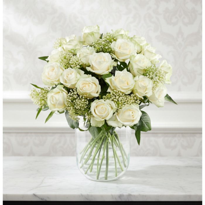 Arreglo floral Estefanía con 24 rosas blancas frescas en un jarrón de cristal sobre una mesa de mármol, con un fondo elegante