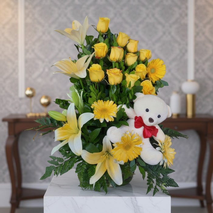 Arreglo floral exótico Amaretto con rosas amarillas, lirios blancos y gerberas, acompañado de un oso de peluche blanco con la