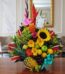Arreglo floral exótico Antídoto con girasoles, heliconias, gladiolos, piña, uvas, peras y manzanas sobre mesa de madera pulid