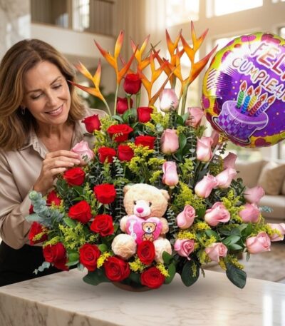 Mujer elegante admira un arreglo floral exótico con rosas rojas y rosadas, aves del paraíso, un oso de peluche y un globo de