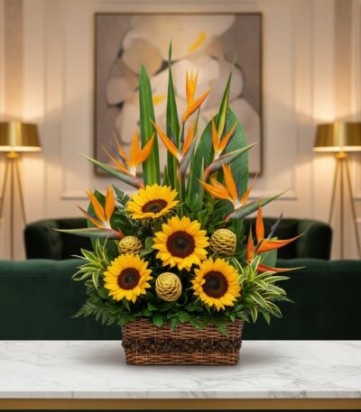 Arreglo floral Fantasía con girasoles vibrantes, exóticas aves del paraíso y detalles verdes en cesta de mimbre, sobre mesa d