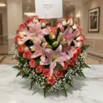 Arreglo floral Feliz Contigo con lirios rosados y rosas bicolor sobre mesa de mármol, fondo elegante de lobby de hotel boutiq