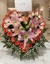 Arreglo floral Feliz Contigo con lirios rosados y rosas bicolor sobre mesa de mármol, fondo elegante de lobby de hotel boutiq