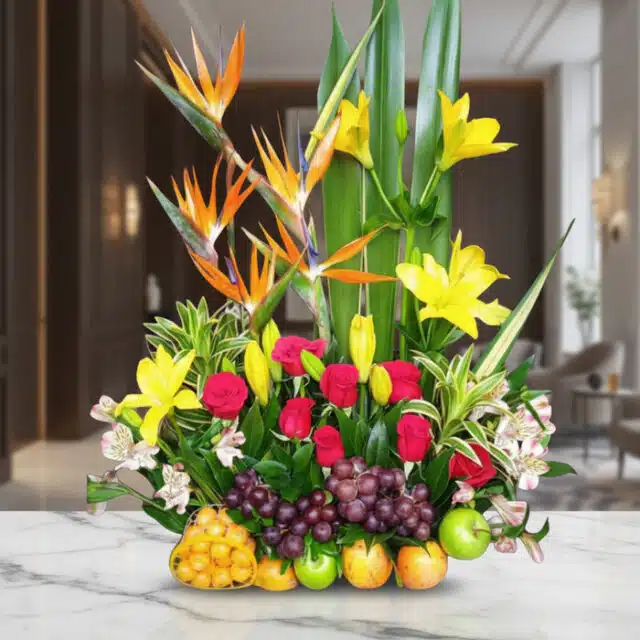 Arreglo floral Akebia con aves del paraíso, lirios amarillos, rosas rojas, uvas y manzanas verdes sobre mármol blanco en un l