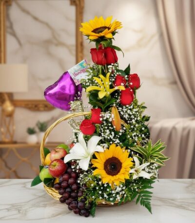 Arreglo floral Capella con girasoles, rosas rojas, lirios blancos y amarillos, y follaje verde, acompañado de una cesta con u