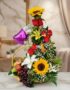 Arreglo floral Capella con girasoles, rosas rojas, lirios blancos y amarillos, y follaje verde, acompañado de una cesta con u