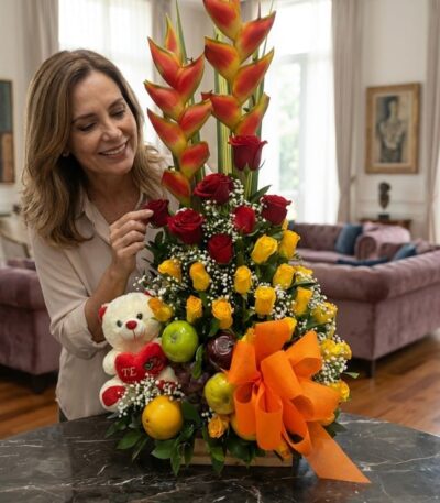 Mujer elegante admirando un Arreglo Floral con Frutas Encanto, compuesto por rosas rojas y amarillas, heliconias, frutas fres