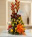 Arreglo floral premium con rosas rojas y amarillas, heliconias, frutas frescas y un lazo naranja, sobre una mesa de mármol en