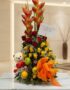 Arreglo floral premium con rosas rojas y amarillas, heliconias, frutas frescas y un lazo naranja, sobre una mesa de mármol en