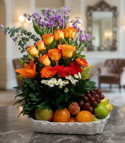 Arreglo floral Hadar con rosas naranjas, lirios, gerberas y margaritas, acompañado de frutas frescas como uvas, manzanas, nar