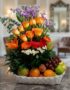 Arreglo floral Hadar con rosas naranjas, lirios, gerberas y margaritas, acompañado de frutas frescas como uvas, manzanas, nar