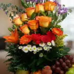 Primer plano extremo del Arreglo Floral con Frutas Hadar, mostrando rosas naranjas, gerberas rojas y margaritas blancas con g