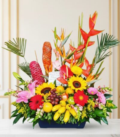 Arreglo floral exótico con heliconias, girasoles, lirios, anturios y frutas tropicales como plátanos, uvas, manzanas y limone