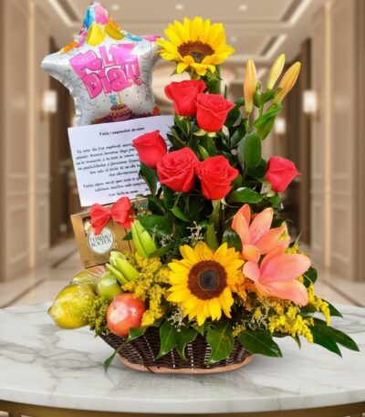 Arreglo floral premium con rosas rojas, girasoles, lirios, frutas kiwano y globo 'Feliz Día' sobre mesa de mármol en lobby el