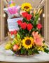 Arreglo floral premium con rosas rojas, girasoles, lirios, frutas kiwano y globo 'Feliz Día' sobre mesa de mármol en lobby el