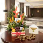 Arreglo floral exótico con flores de ave del paraíso y heliconias, piñas, uvas, manzanas y naranjas, acompañado de una botell