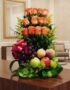 Arreglo floral premium con rosas salmón, uvas, manzanas, duraznos y peras, sobre una mesa de madera pulida en un lobby de hot
