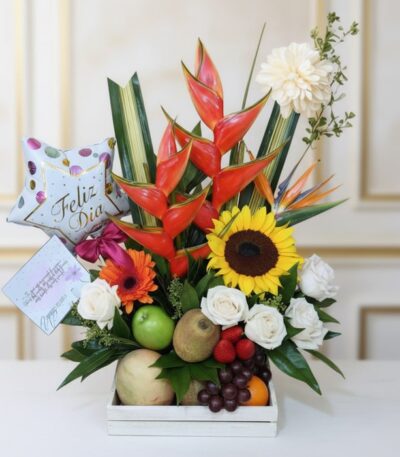 Arreglo floral con frutas tamarillo, girasoles, rosas blancas, heliconias y globo 'Feliz Día' en base de madera, ideal para e