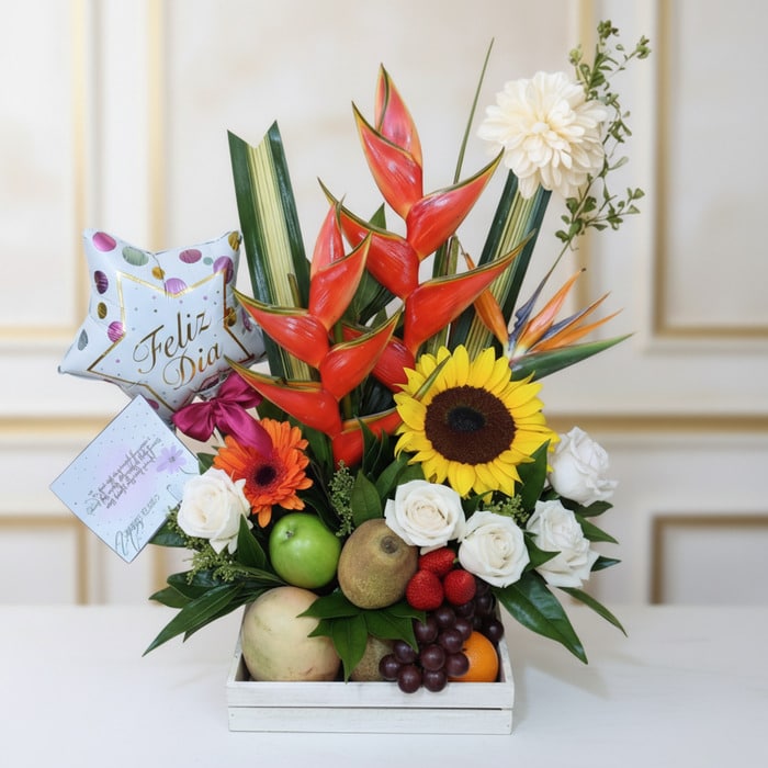 Arreglo floral con frutas tamarillo, girasoles, rosas blancas, heliconias y globo 'Feliz Día' en base de madera, ideal para e