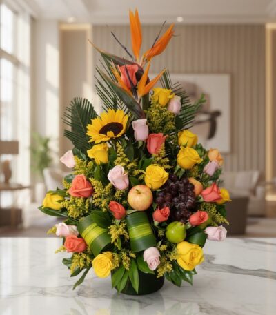 Arreglo floral vibrante con rosas amarillas y salmón, girasol, ave del paraíso y frutas tropicales como uvas, manzana y lima,