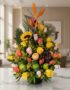Arreglo floral vibrante con rosas amarillas y salmón, girasol, ave del paraíso y frutas tropicales como uvas, manzana y lima,