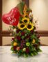 Arreglo floral premium con girasoles, rosas rojas, frutas tropicales (uvas, manzanas, naranjas) y un globo rojo de corazón co