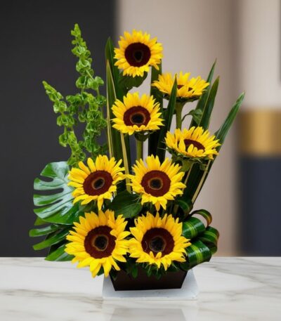 Arreglo floral premium con girasoles Bengala, hojas verdes y follaje, sobre una mesa de mármol en un lobby de hotel boutique.