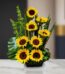 Arreglo floral premium con girasoles Bengala, hojas verdes y follaje, sobre una mesa de mármol en un lobby de hotel boutique.